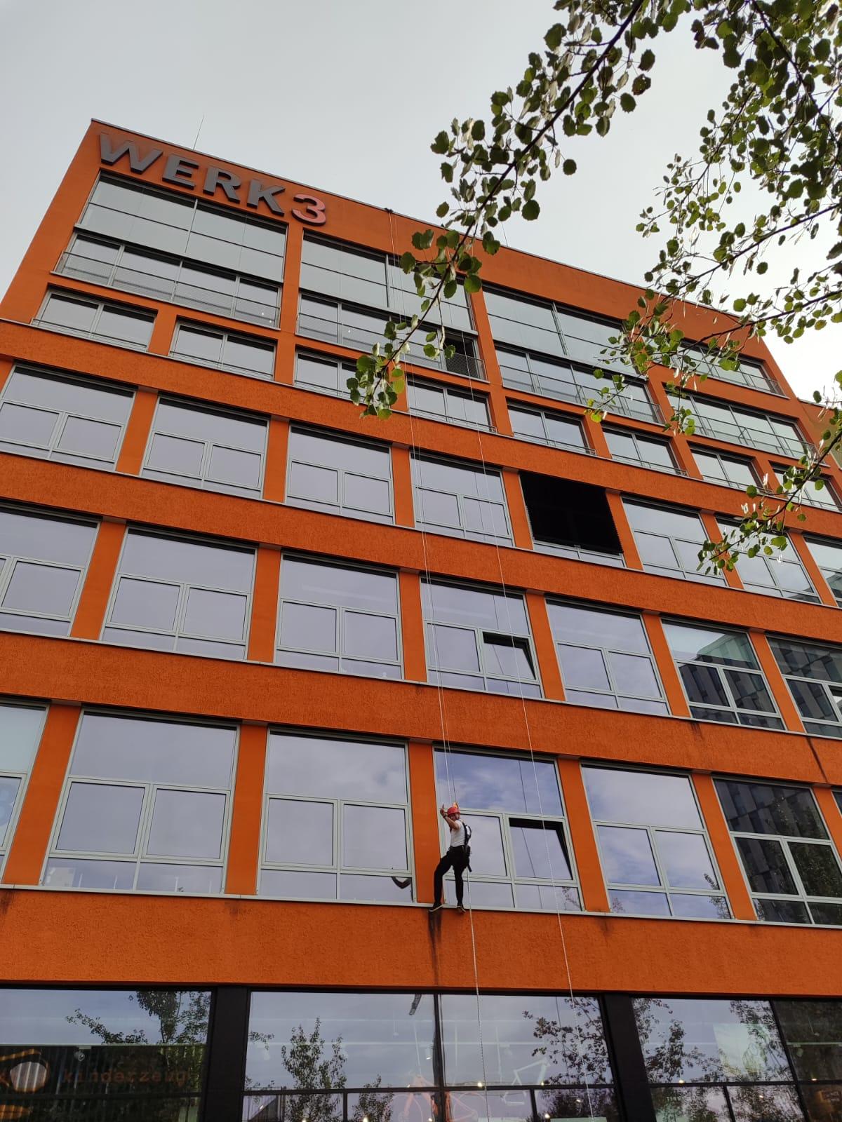 Industriekletterer an einer orangefarbenen Gebäudefassade